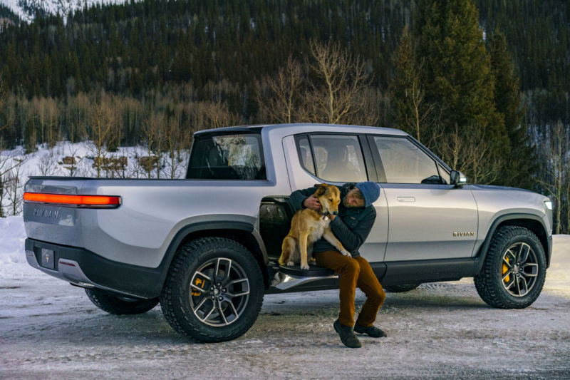 A man and a dog sit on an electric pickup truck