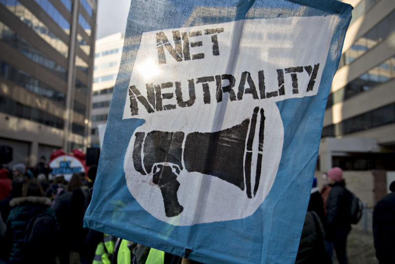 A protestor holds a sign with a picture of a bullhorn and the words, 