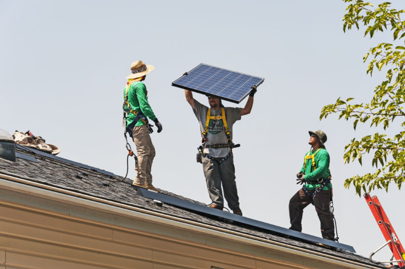 Men on roof, one holding solar panel.