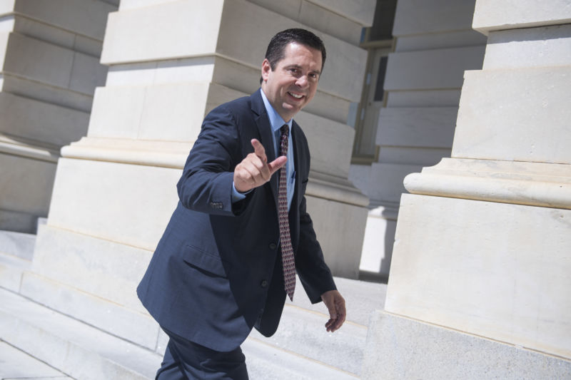 A man in a suit points and smiles as he walks inside a building.