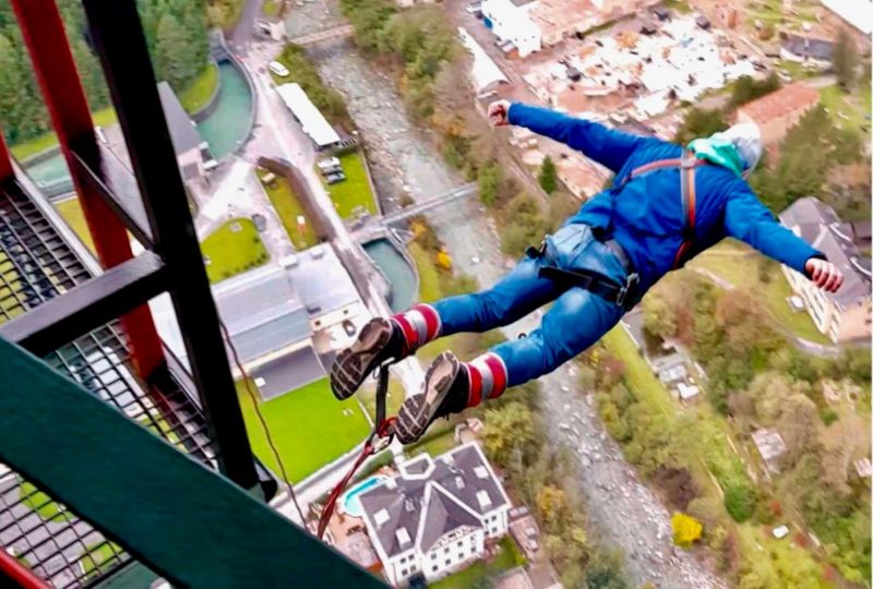 A man bungee jumps from a metal bridge toward the village below him.