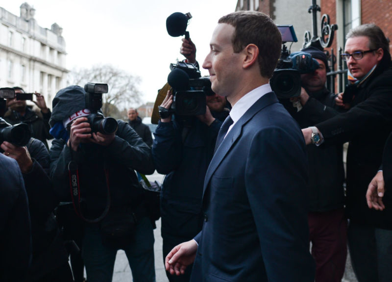 Facebook CEO Mark Zuckerberg wearing a suit and being photographed by several photographers as he leaves a hotel.