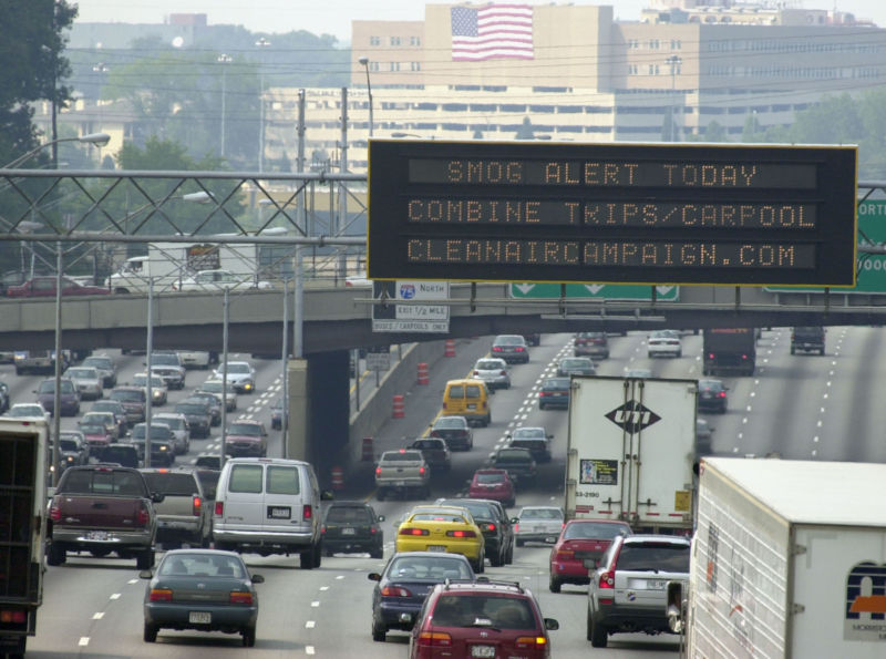 Traffic underneath a smog alert sign.