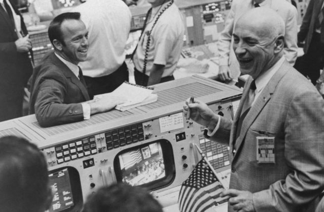 Cigars and US flags dot the Mission Control Center in Houston on May 26 after successful completion of the Apollo 10 Moon mission. Among the celebrants are Alan Shepard (left), who was the first US man in space, and Robert Gilruth (right), Director of the Space Center.