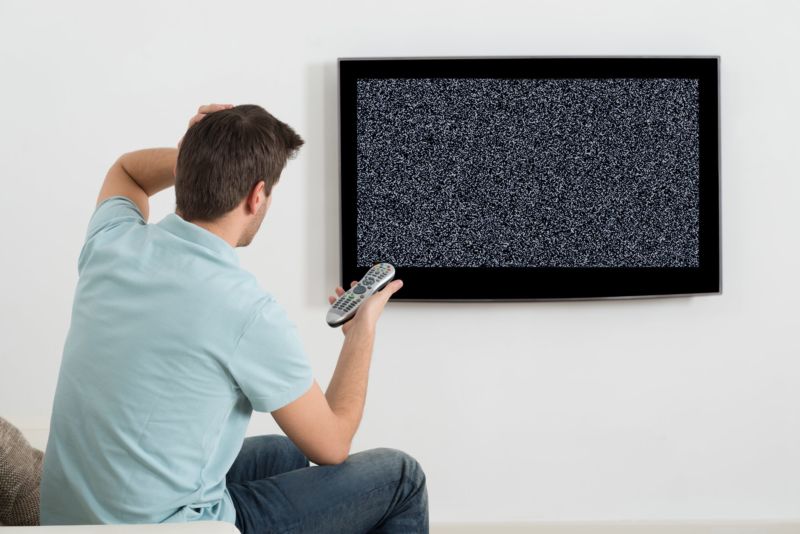 A man sitting in front of a TV that shows only static.