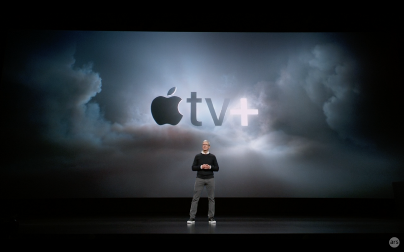 A man in business casual gives a presentation in front of a monstrous video screen.