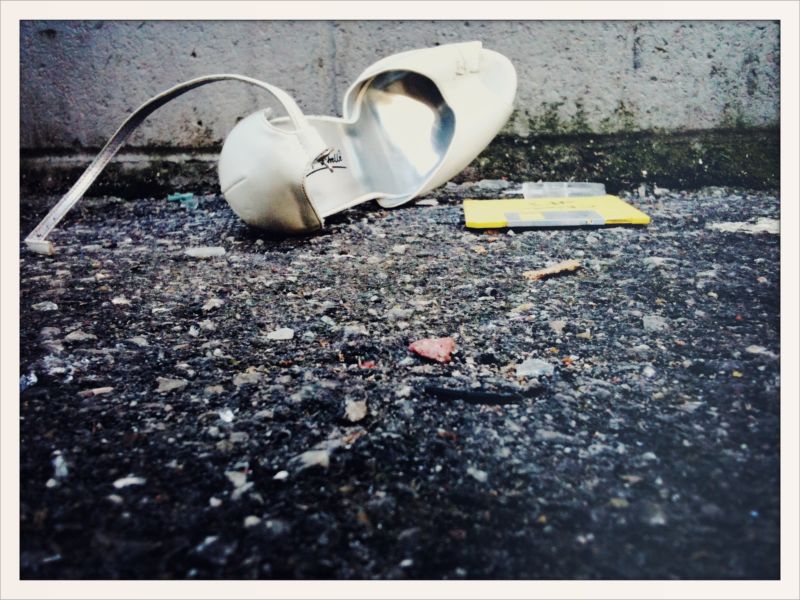 A high-heeled shoe and a floppy disk sit next to each other on gravel.