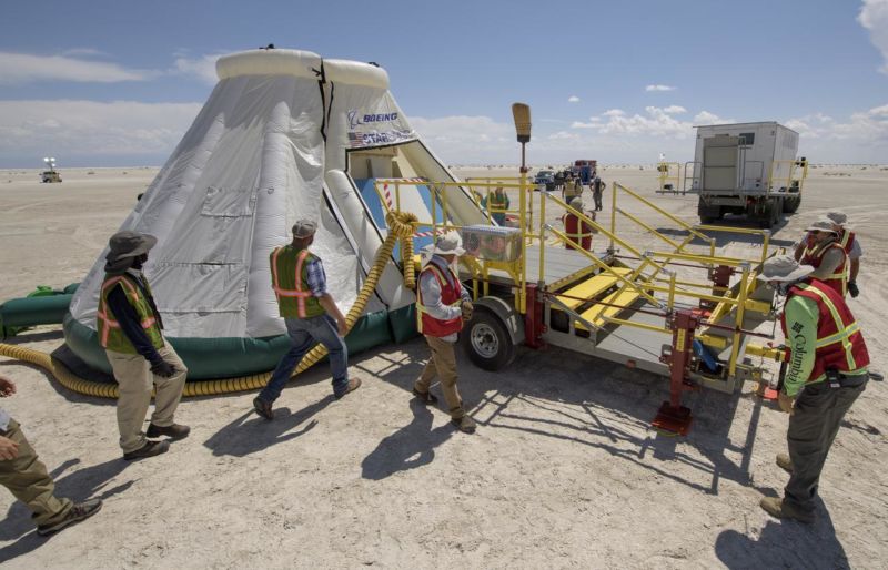 People in safety gear work on a spacecraft mockup in the desert.