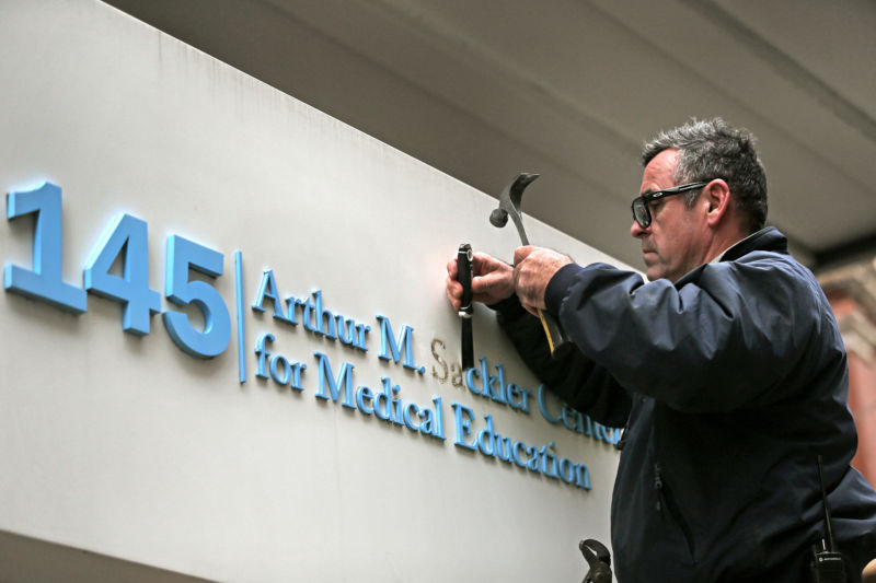 BOSTON, MA - DECEMBER 5: Tufts employee Gabe Ryan removes letters from signage featuring the Sackler family name at the Tufts building at 145 Harrison Ave. in Boston on Dec. 5, 2019. 