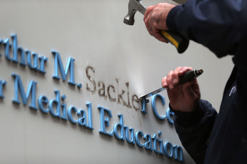 Closeup of hands with a hammer and chisel removing letters from a wall.