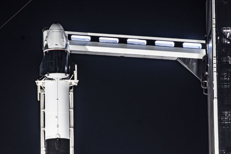 The Crew Dragon spacecraft sits atop a Falcon 9 rocket, with the crew access arm extended.