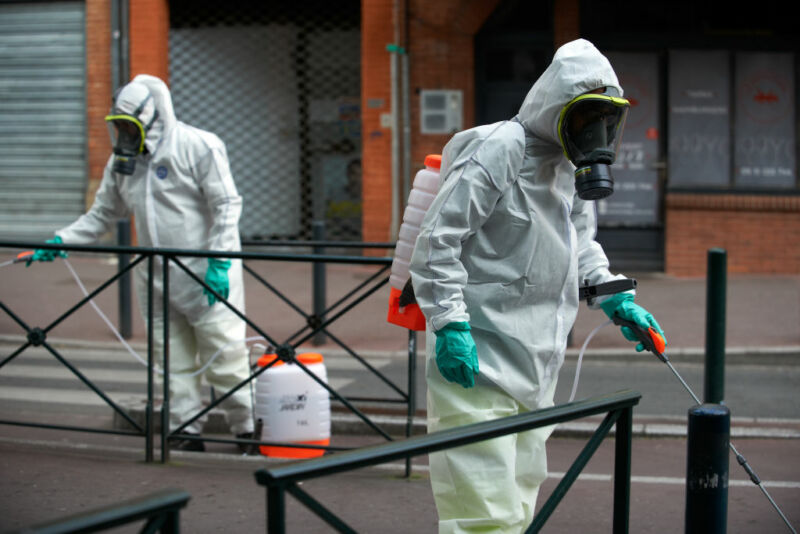 Image of two men in protective clothing spraying a public area.