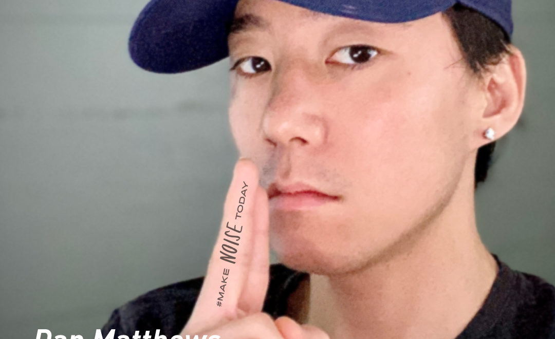 an asian man in a hat with a finger up to his lips