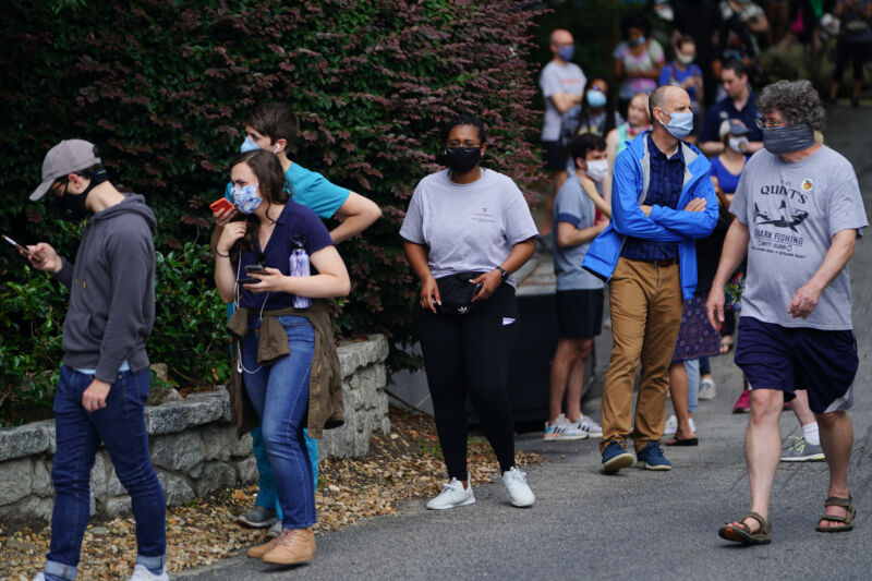 Bored people in masks wait in line.