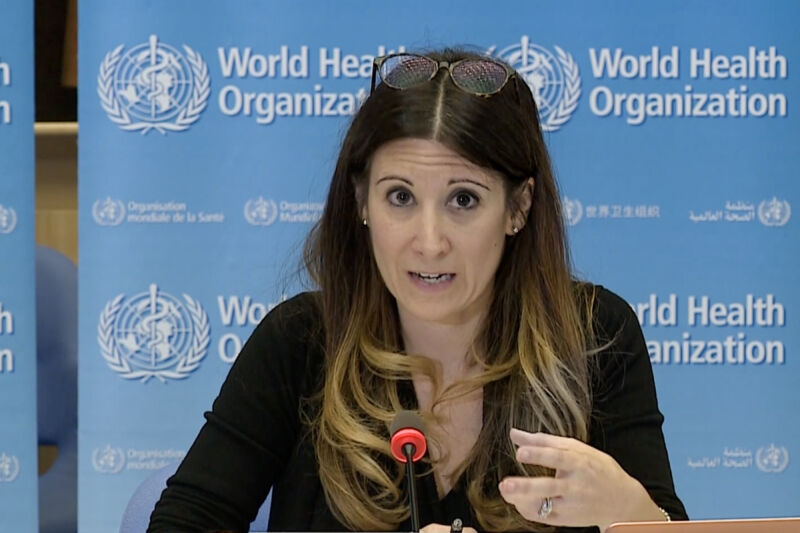 A women speaks into a microphone in front of a World Health Organization logo.