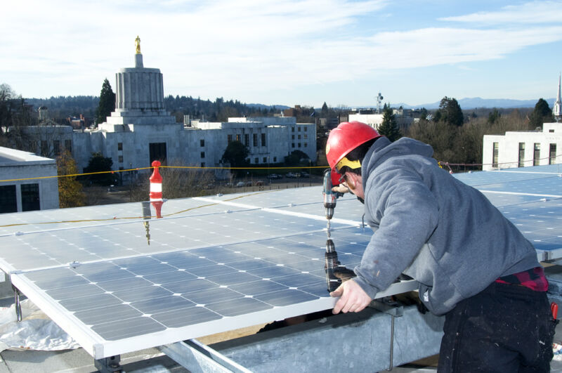 Workers in hardhats install rooftop solar panels.