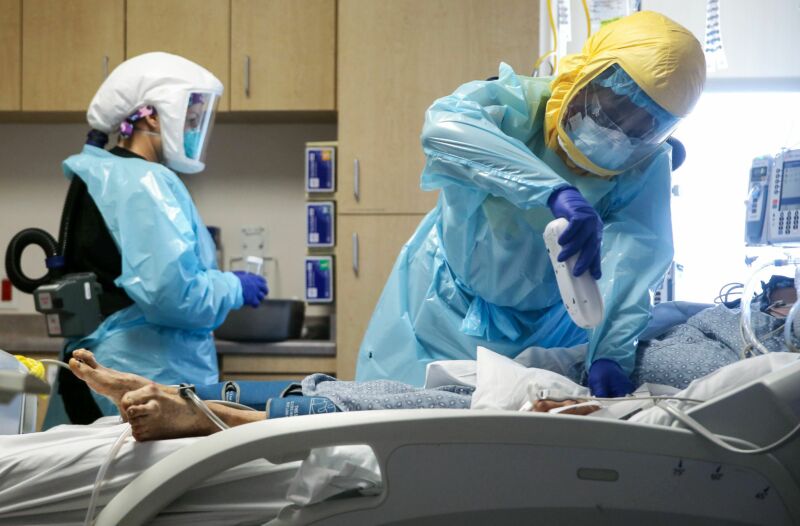 A patient is attended to by two people in protective gear, including breathing apparatus.