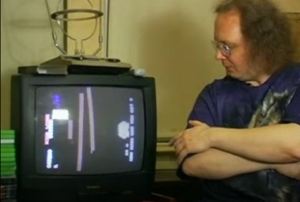 Former Twin Galaxies referee Robert Mruczek sits next to taped footage of a Mitchell performance showing the telltale "girder finger" in a 2006 MTV News interview.