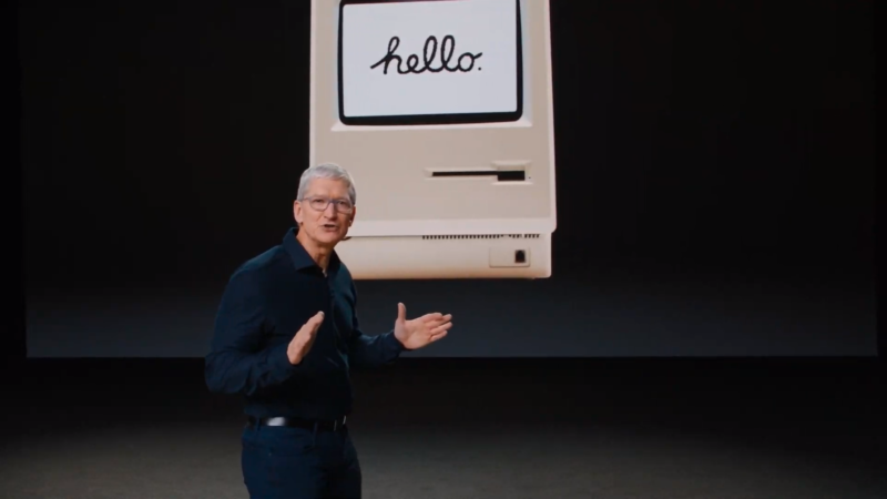 A man gives a presentation in front of an image of a late 20th century computer.