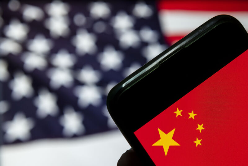 An American flag is out of focus behind a smartphone showing an image of the Chinese flag.