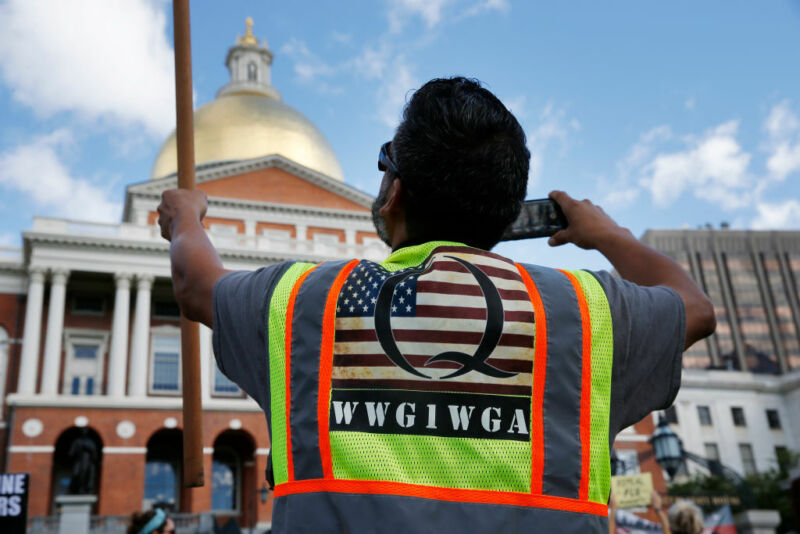 BOSTON—A man wearing a QAnon vest held a flag during a No Mandatory Flu Shot Massachusetts rally held outside of the State House in Boston on Aug. 30, 2020, to demonstrate against Gov. Charlie Baker's order for mandatory influenza vaccinations for all students under the age of 30, an effort to lower the burden on the health care system during the COVID-19 pandemic.