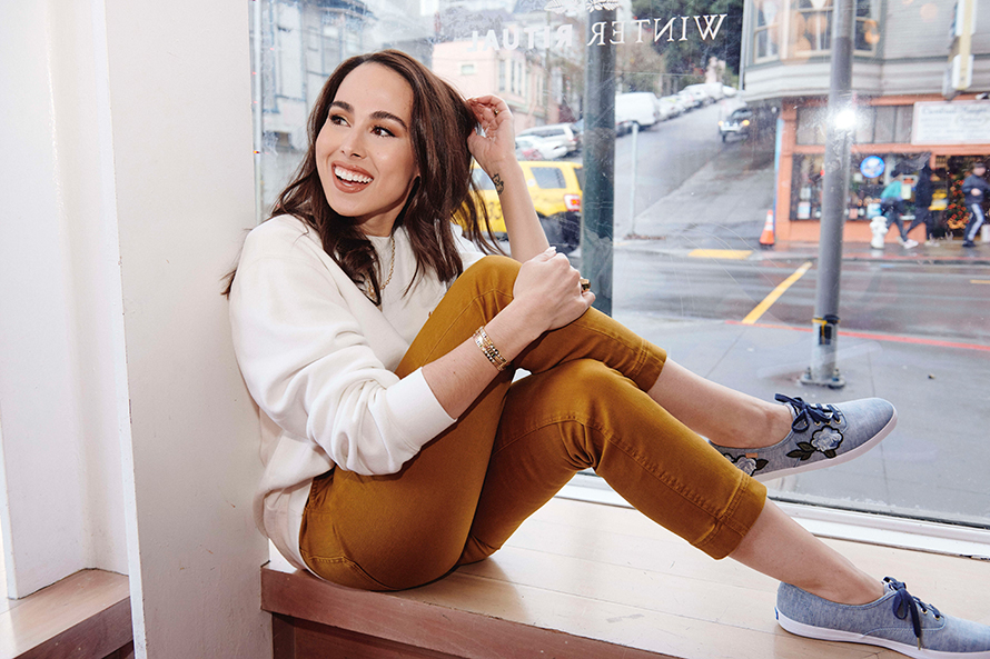 a woman with brown hair smiling while sitting in a store window