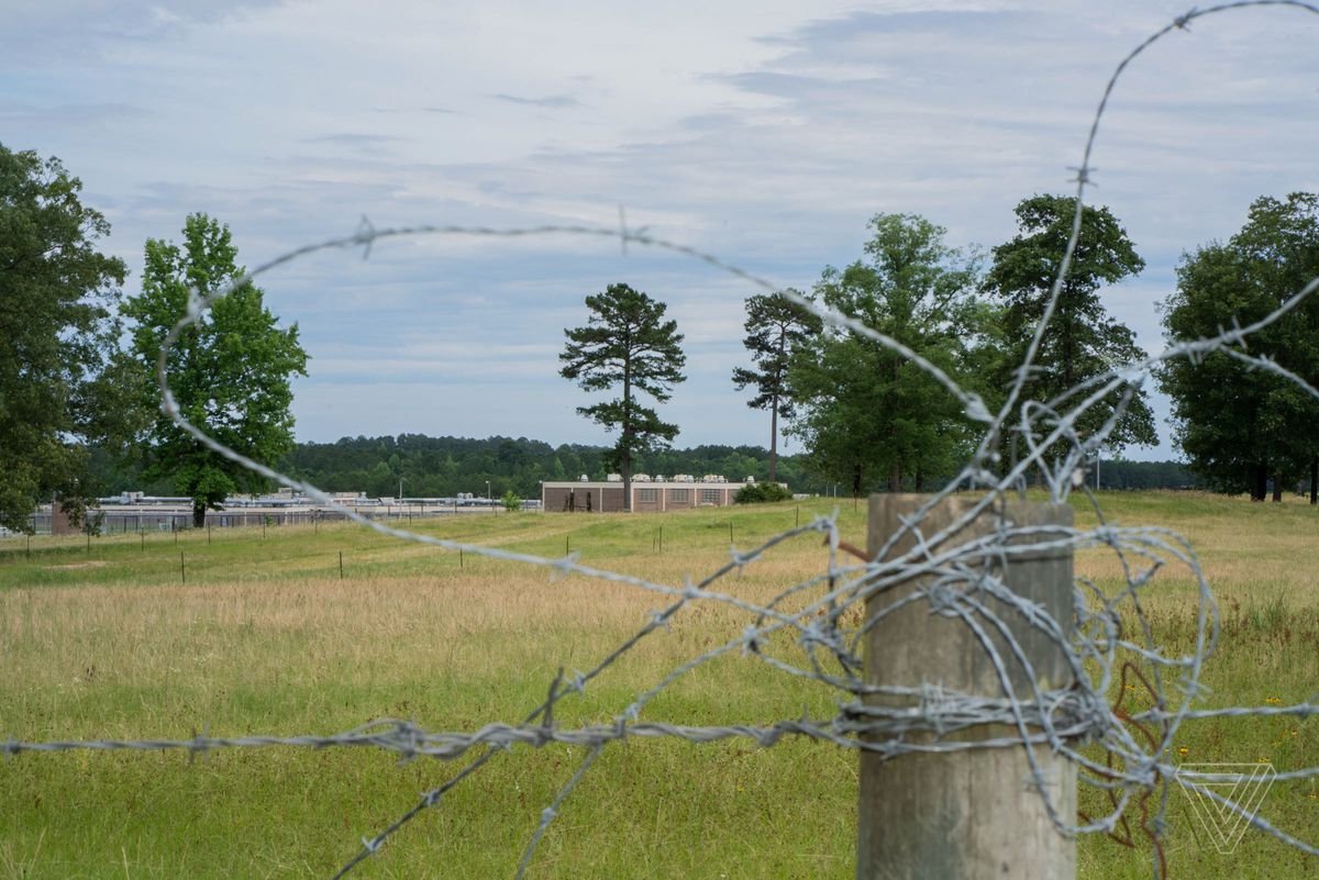 Winn Correctional Facility seen through barbed wire on a wooden fence post.