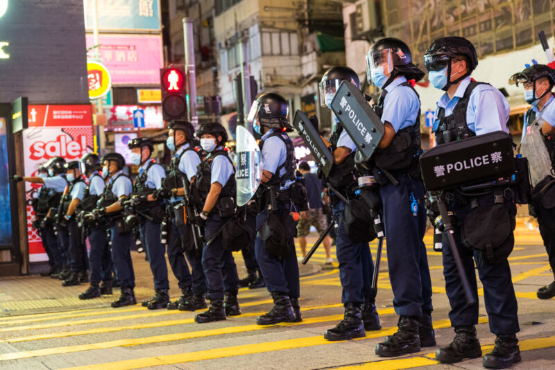 Police in riot gear crowd an urban crosswalk.