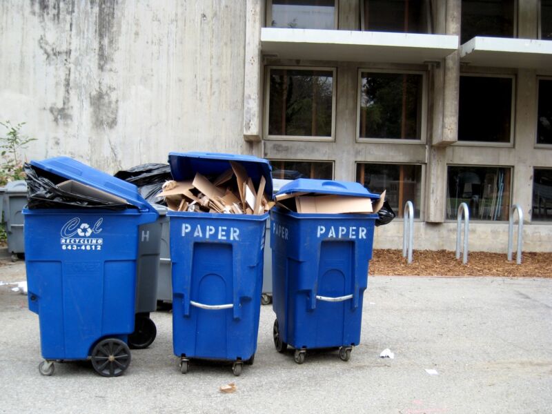 A row of blue paper recycling bins stuffed with cardboard.