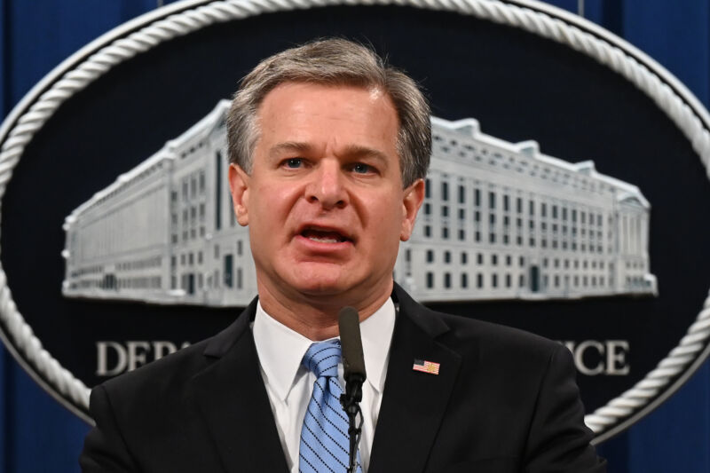 A man in a suit speaks in front of a Justice Department logo.