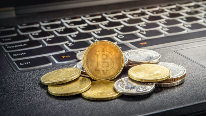 A pile of coins with the bitcoin logo sits atop a laptop keyboard.