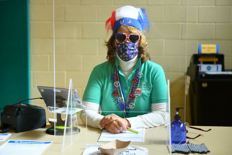 A masked woman in red, white, and blue flare sits at a desk.