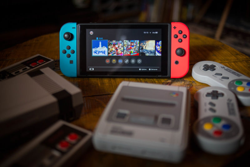 a Nintendo Switch (M) surrounded by a NES (Nintendo Entertainment System) Classic Mini (L) and a SNES (Super Nintendo Entertainment System) Classic Mini (R) video game consoles.