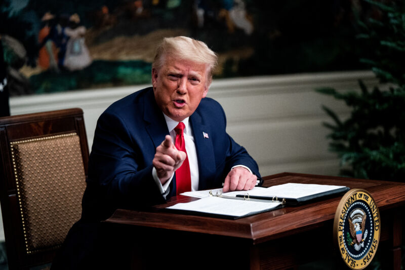 A man in a suit points from a small desk.