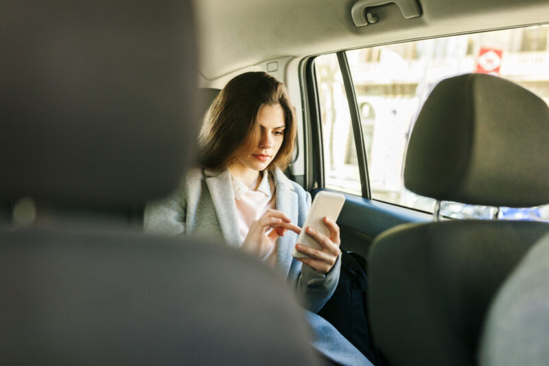 Young businesswoman sitting on backseat of a car using cell phone