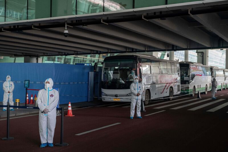 Health workers in personal protection suits stand next to buses at a cordoned-off section of the international airport in Wuhan on January 14, 2021, following the arrival of a World Health Organization (WHO) team investigating the origins of the COVID-19 pandemic.