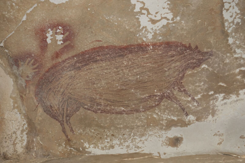 Color photo of stylized pig painted in red on a rock wall