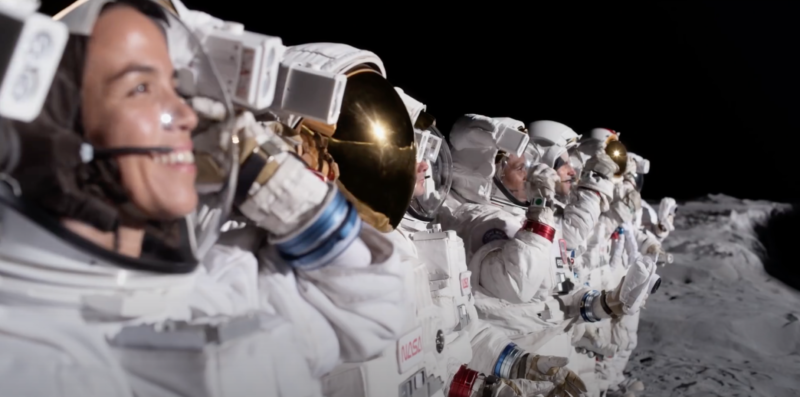 Astronauts stand in a row on the lunar surface.