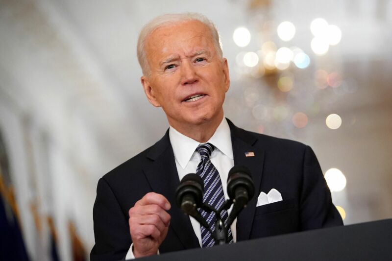 An older man in a suit speaks into a microphone on a podium.