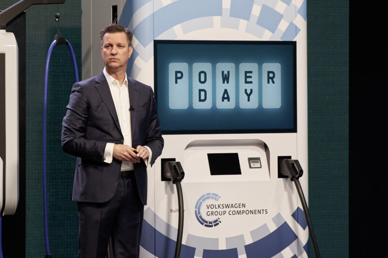 A man in an open-collared suit stands in front of a large power charger mockup.