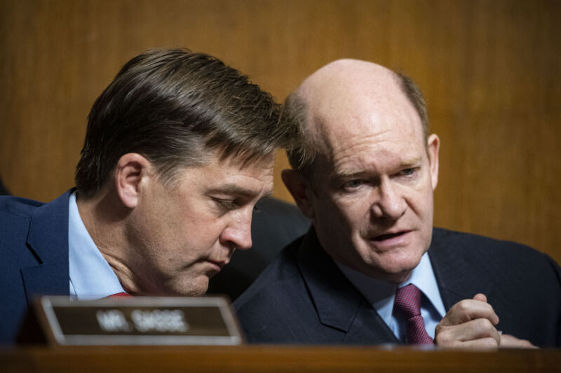 Two serious men in suits talk amongst themselves.