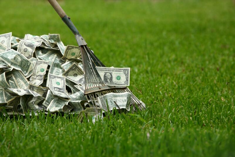 A rake being used to gather a pile of money on a lawn.