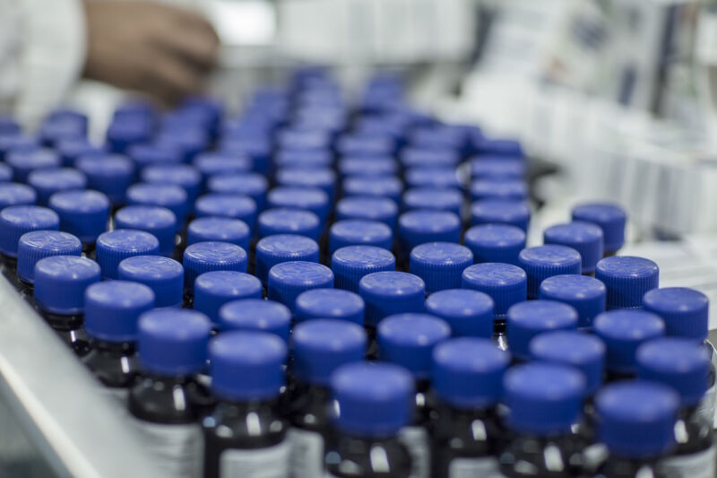 Tiny bottles with plastic lids crowd a conveyor belt.