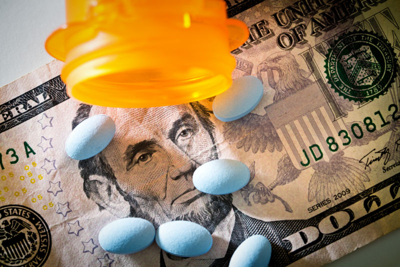 High angle close-up view still life of an opened prescription bottles with pills and medication spilling onto ae background of money, U.S. currency with Lincoln Portrait.