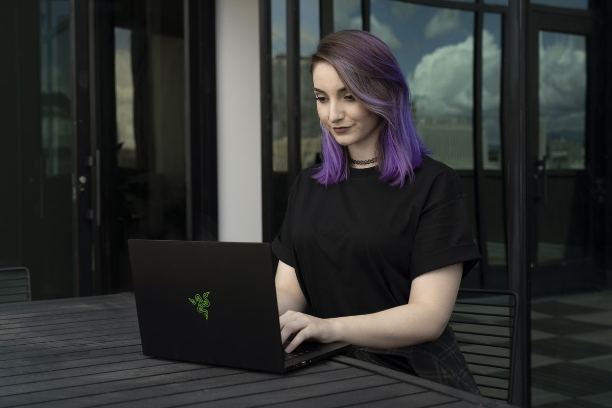 A user sits at an outdoor picnic table, typing on the Razer Blade 14.