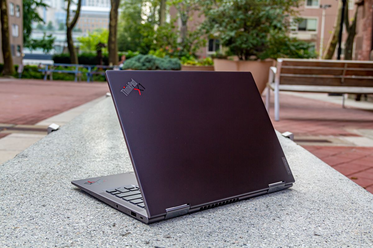 The ThinkPd X1 Yoga Gen 6 half open, angled to the left, seen from behind on a stone bench outdoors.