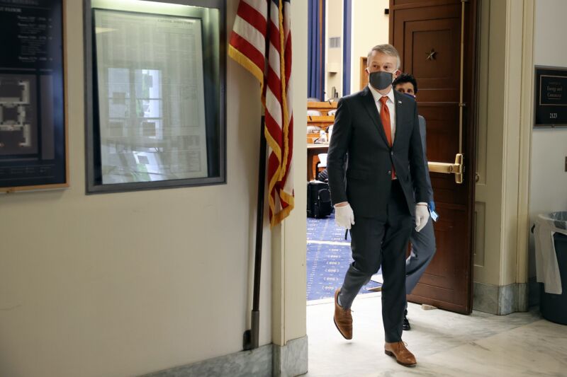 Rick Bright walks out of a hearing room, wearing a face mask and gloves.