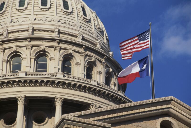 US and Texas flags in front of the Texas state capitol building.