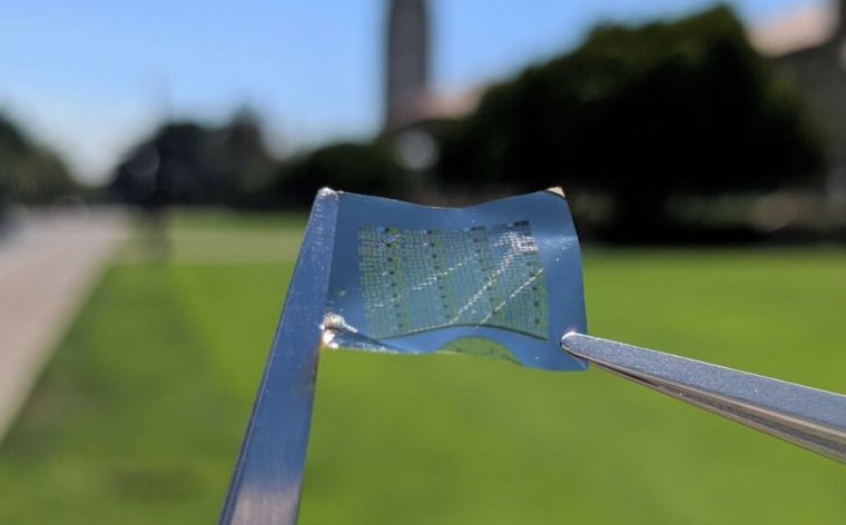 Extreme close-up photograph of tweezers holding a flexible computer component.