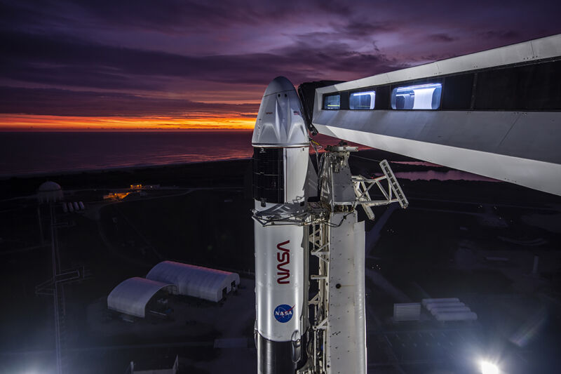 A rocket sits on a launch pad during a purple- and gold-streaked dawn.